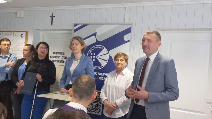 Pokaż zdjęcie: W jednym z pomieszczeń placówki, trwa uroczyste otwarcie, goście gratulują otwarcia. Na zdjęciu zarząd placówki i goście stoją w jednym rzędzie.