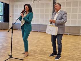 Pokaż zdjęcie: Kobieta i mężczyzna na środku sali przemawiają do mikrofonu