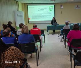 Pokaż zdjęcie: Zdjęcie z tyłu sali konferencyjnej w kierunku prelegenta. Na ekranie slajd z prezentacji.