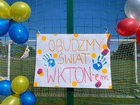 Transparent, powieszony na płocie, z napisem "Obudźmy świat WKTON-em i odciskami dłoni, wokół kolorowe balony