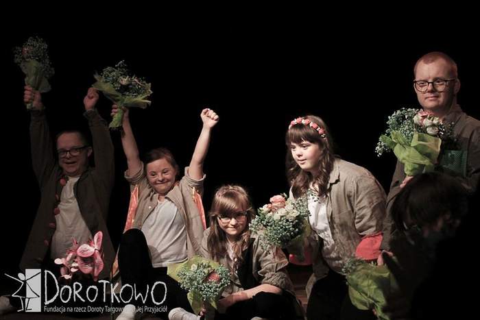 Aktorzy teatru "TAK czy NIE" stoją na scenie, trzymając w ręku bukiety kwiatów