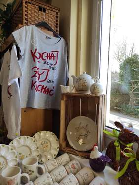 Pokaż zdjęcie: Ceramika ozdobiona akcentami wielkanocnymi została ułożona w sąsiedztwie okna. Na wieszaku wisi również koszulka z napisem: „Kochaj, żeby żyć. Żyj, żeby kochać”. 