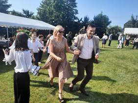 Pokaż zdjęcie: Na trawie tańczą ludzie. Są dobrani w pary i pląsają w kółku. 