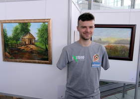 Pokaż zdjęcie: Bartosz Ostałowski na tle prac prezentowanych na wystawie