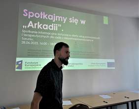 Pan Hubert Kasprzak podczas prelekcji, w tle sjald "Spotkajmy się w "Arkadii""