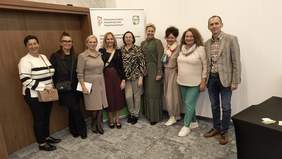 Pokaż zdjęcie: Zdjęcie grupowe części gości na tle rollupów. Widzimy uśmiechnięte osoby - uczestników konferencji.