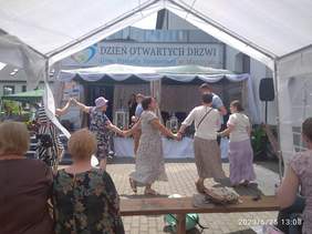 Pokaż zdjęcie: Podczas Dni otwartych na zewnątrz przed budynkiem DPS trwają zabawy i tańce, zdjęcie przedstawia bawiące, tańczące osoby