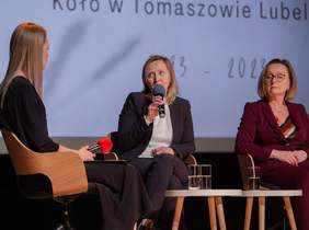 Pokaż zdjęcie: Panel ekspercki podczas gali, na scenie ustawiono krzesła, na których siedzą goście i rozmawiają, zdjęcie trzech kobiet podczas panelu, przy mikrofonie blondynka w ciemnym garniturze