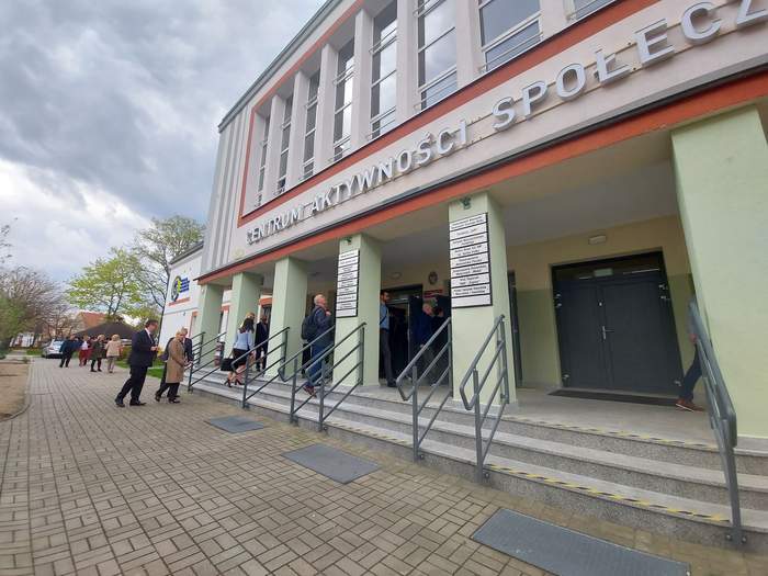 Pokaż zdjęcie: Osoby wchodzą do budynku Centrum Aktywności Społecznej w Nowej Soli, są na schodach i przed wejściem, kobiety i mężczyźni