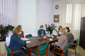 Pokaż zdjęcie: Sześć kobiet siedzących w maseczkach przy brązowym stole, przed nimi leżą dokumenty