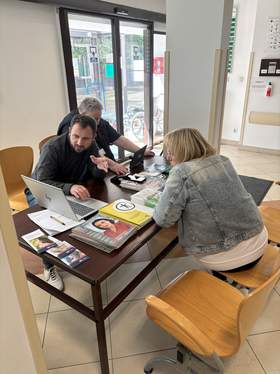Dwóch pracowników PFRON rozmawia. Kobieta i mężczyzna patrzą na ekran laptopa znajdującego się na stole, omawiając przekazywane informacje. Na stanowisku widoczne są również materiały informacyjne PFRON.