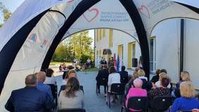 Pokaż zdjęcie: Zebrani na uroczystości goście podczas przemówienia dyrektor Marty Mordarskiej. Uczestnicy siędzą na krzesłach pod namiotem