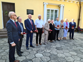 Pokaż zdjęcie: Przed budynkiem w rzędzie stoi 10  osób, w rękach trzymają okolicznościowe medale.