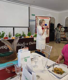 Pokaż zdjęcie: Kobieta stoi w dłoni trzyma mikrofon, przemawia.  