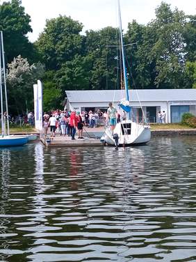 Pokaż zdjęcie: Zdjęcie żaglówki przy molo, na którym czekają pasażerowie.
