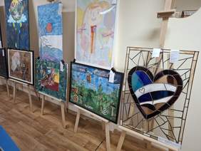 Przestronna sala. Wzdłuż ścian rozmieszczono wiele obrazów na sztalugach.