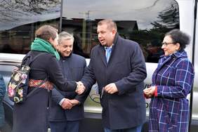 Pokaż zdjęcie: Na tle busa stoją dwie kobiety i dwóch mężczyzn, jeden z nich wręcza kobiecie kluczyki do samochodu.