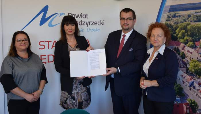 Pokaż zdjęcie: Dyrektor Oddziału wraz ze Starostą Międzyrzeckim oraz Wicestarostą i pracownikiem PCPR na tle ścianki promocyjej Powiatu z podpisaną umową