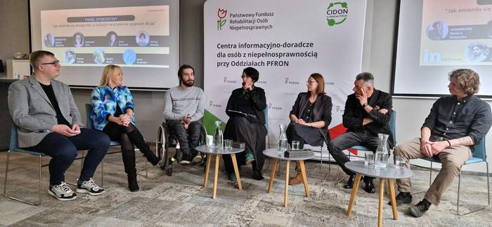 Pokaż zdjęcie: Paneliści kobiety i mężczyźni siedzą na środku sali na krzesłach. Dyskusję moderuje kobieta. Wśród panelistów są osoby z niepełnosprawnościami.