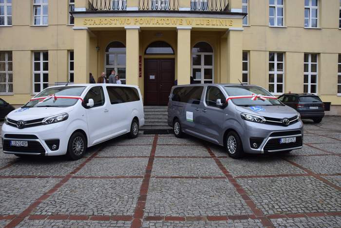 Pokaż zdjęcie: Przed budynkiem starostwa powiatowego w Lublinie stoją dwa nowe busy, jeden w kolorze grafik metalic, drugi w kolorze białym. Obydwa busy są marki Toyota 