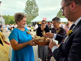 Pokaż zdjęcie: Kobieta w niebieskiej sukience roznosi gościom kawałki chleba zgodnie z dożynkową tradycją.