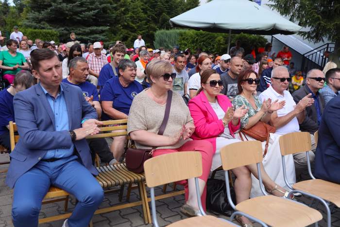 Pokaż zdjęcie: Zdjęcie zaproszonych gości siedzących na krzesłach w plenerze. 