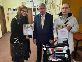 Pokaż zdjęcie: Do zdjęcia pozują trzy osoby: dyrektor Łódzkiego Oddziału PFRON, zwycięzca konkursu plastycznego i terapeutka zajęciowa. W dłoniach trzymają pamiątkowe dyplomy i bardzo duży zestaw artystyczny. 
