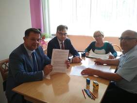 Pokaż zdjęcie: Cztery osoby siedzące przy stoliku podpisujące dokumenty