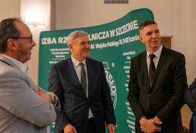 Pokaż zdjęcie: Grupa uczestników Spotkania Opłatkowo-Noworocznego w Szczecinie podczas rozmowy. W tle widoczny baner Izby Rzemieślniczej w Szczecinie, symbolizujący zaangażowanie organizacji w działalność na rzecz rzemiosła.