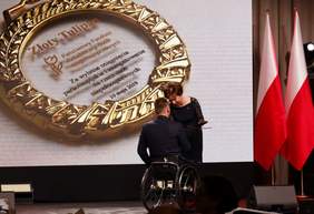 Pokaż zdjęcie: Prezes Maląg wręcza Złotego Tulipana siedzącemu na wózku sportowcowi, Grzegorzowi Plucie
