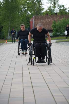 Pokaż zdjęcie: Dwóch młodych mężczyzn ściga się na wózkach inwalidzkich 