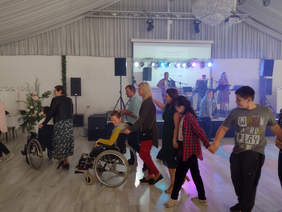 osoby przed sceną tańczą, w rzędzie, w tym 2 osoby na wózku inwalidzkim