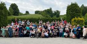 Pokaż zdjęcie: Na zdjęciu ponad sto uśmiechniętych osób stoi na tle lasu
