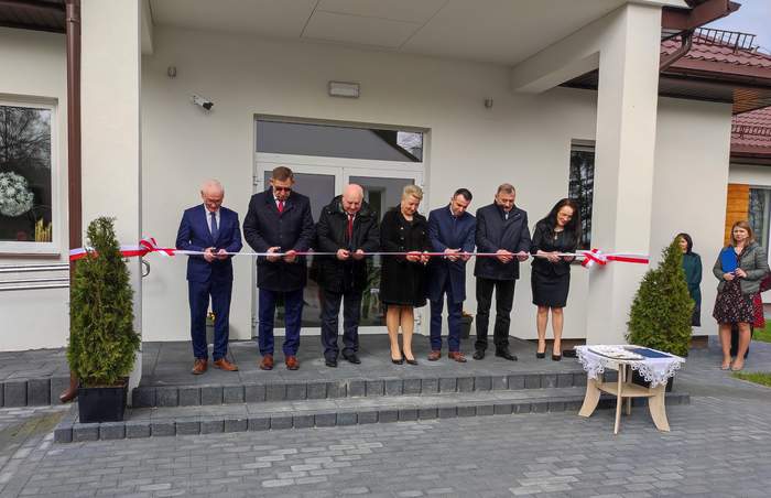 Pokaż zdjęcie: Przy wejściu do budynku, sześć osób przecina uroczyście wstęgę
