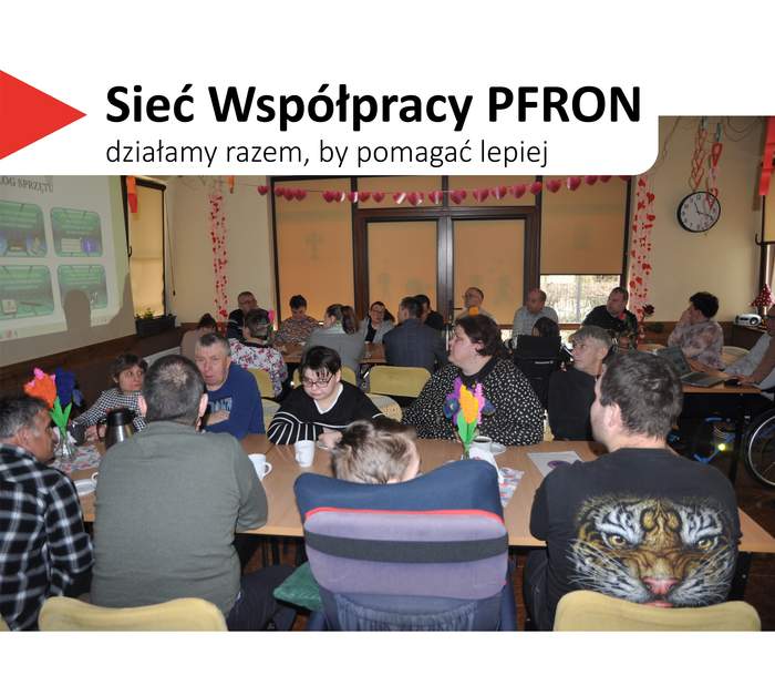 Pokaż zdjęcie: Sala wypełniona dorosłymi uczestnikami siedzącymi przy stołach, zwróconymi w stronę prowadzącego. W lewym górnym rogu widnieje hasło „Sieć Współpracy PFRON – działamy razem, by pomagać lepiej”.