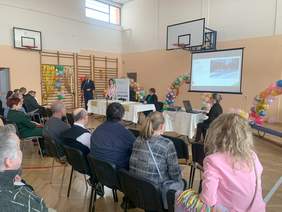 uczestnicy gali, widok z tyłu, widać siedzące osoby, na ekranie wyświetlane są informacje o pracach, dyrektor wręcza nagrody