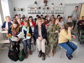 Pokaż zdjęcie: Duża grupa kobiet w różnym wieku. Kobiety siedzą na krzesełkach i oglądają występ.