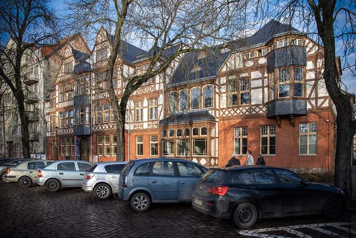 Zabytkowy budynek w tle, przed budynkiem zaparkowane samochody
