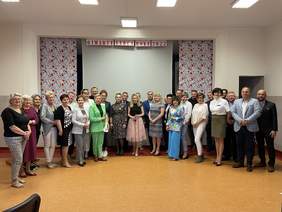 Pokaż zdjęcie: Przed sceną stoi grupa kilkudziesięciu osób. Wszyscy elegancko ubrani. Nad nimi napis „Otwarte Serca Roku 2022”