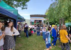 Pokaż zdjęcie: Plac, na którym odbywała się impreza w koło chodzą ludzie w oddali udekorowana scena dla artystów.