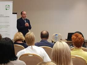 sala konferencyjna, widok siedzących z tyłu, z lewej strony mężczyzna mówi do mikrofonu