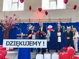 W szkolnej sali gimnastycznej ustawiona jest scena. Stoi na niej dyrektor Łódzkiego Oddziału PFRON, który odbiera nagrodę "Kryształowe Serce". 