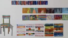 Pokaż zdjęcie: na białej ścianie zawieszone cztery rzędy barwnych obrazów z lewej strony zawieszone jest kolorowe krzesło 
