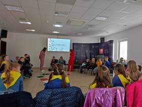 Pokaż zdjęcie: W sali starostwa powiatowego odbywają się warsztaty psychoedukacyjne dla dzieci. Dzieci siedzą na krzesełkach i rozmawiają na temat autyzmu.