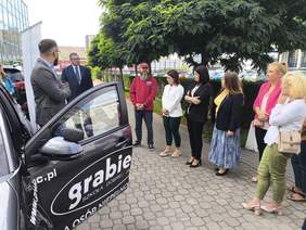 Pokaż zdjęcie: Grupa osób stoi przy otwartym samochodzie.