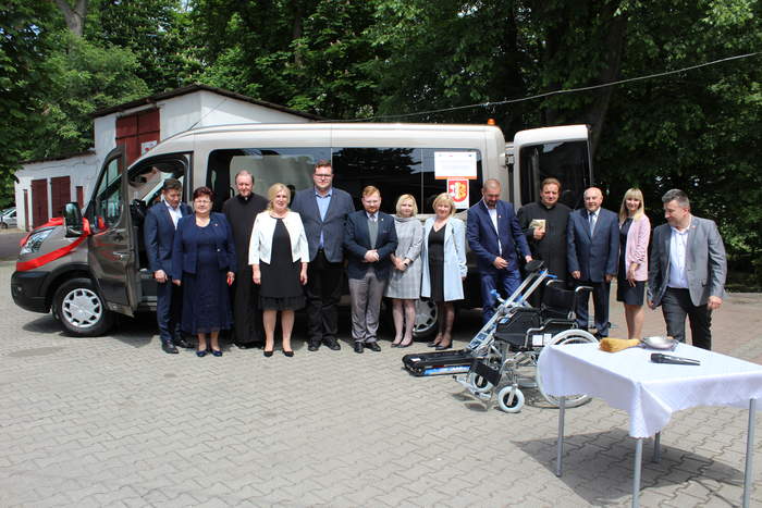 Pokaż zdjęcie: 5 kobiet i 8 mężczyzn na tle nowego busa.Przed zgromadzonymi wóżek inwalidzki,stół z kropidłem