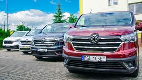 Pokaż zdjęcie: Cztery busy w kolorach: białym, srebrnym, granatowym i wiśniowym stoją zaparkowane przed budynkiem urzędu. W tle widoczne są drzewa, krzewy oraz wysokie metalowe ogrodzenie.