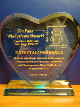 Pokaż zdjęcie: Na biurku stoi statuetka "Kryształowe Serce", którą otrzymał dyrektor Łódzkiego Oddziału PFRON Władysław Skwarka. Są na niej napisane słowa podziękowań za wielkie serce i pomoc niesioną dzieciom. 