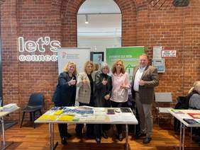 Pokaż zdjęcie: Przy stoisku informacyjnym PFRON stoją przedstawiciele instytucji. Wszyscy są uśmiechnięci i pokazują kciuk w górę. 