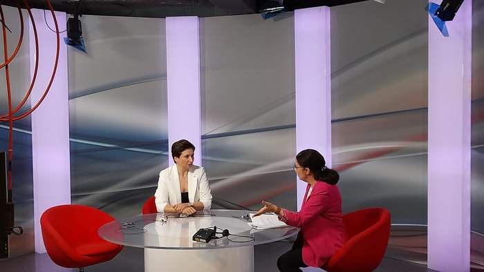 Pokaż zdjęcie: W studiu telewizyjnym TVP3 Lublin, przy szklanym stole siedzą dwie kobiety ubrane w marynarki. Kobieta po lewej stronie z ciemnymi krótkimi włosami, kobieta po prawej stronie z czarnymi włosami związanymi w kucyk.